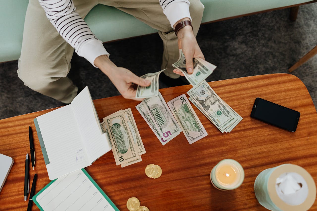 A person sitting and counting various US dollar bills at a table indoors.